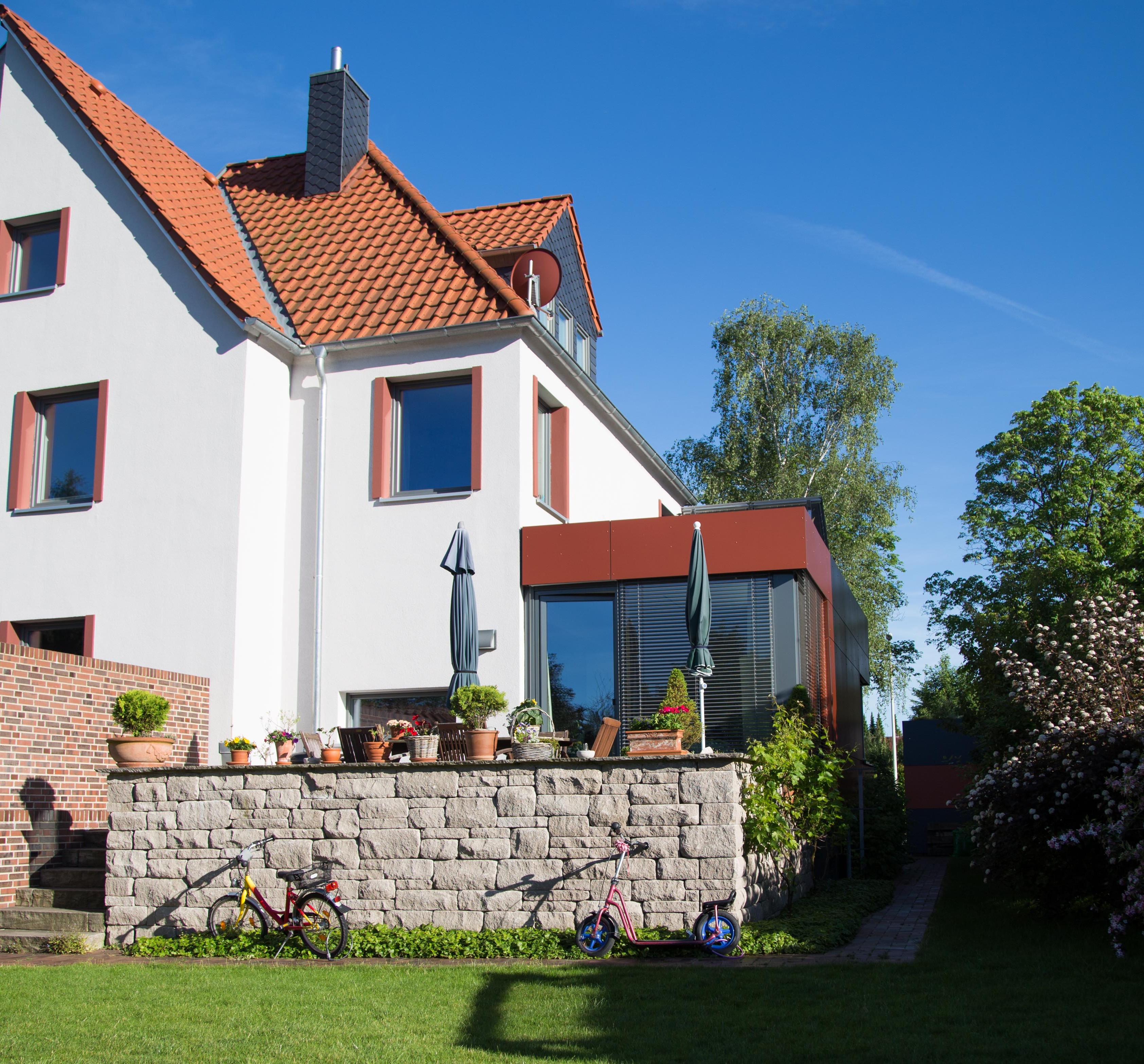 Gartenansicht des Reihenhauses mit Ziegeldach, verglastem Anbau und erhöhter Terrasse